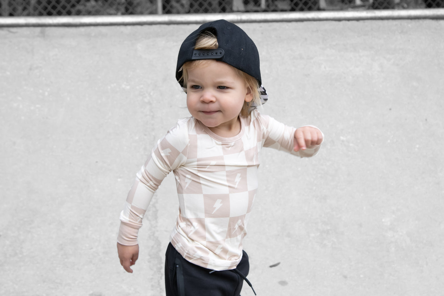 Child wearing a patterned long-sleeve shirt and cap against a plain background