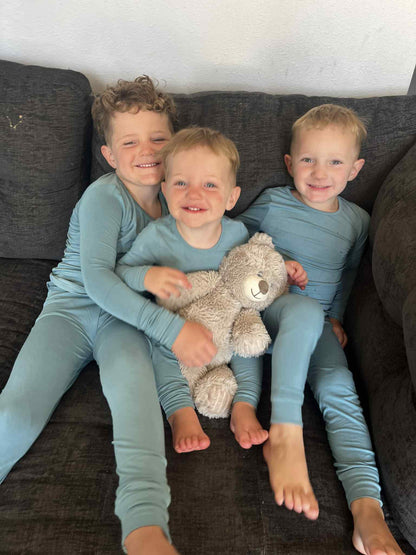 Three children in matching outfits sitting on a couch with a teddy bear.