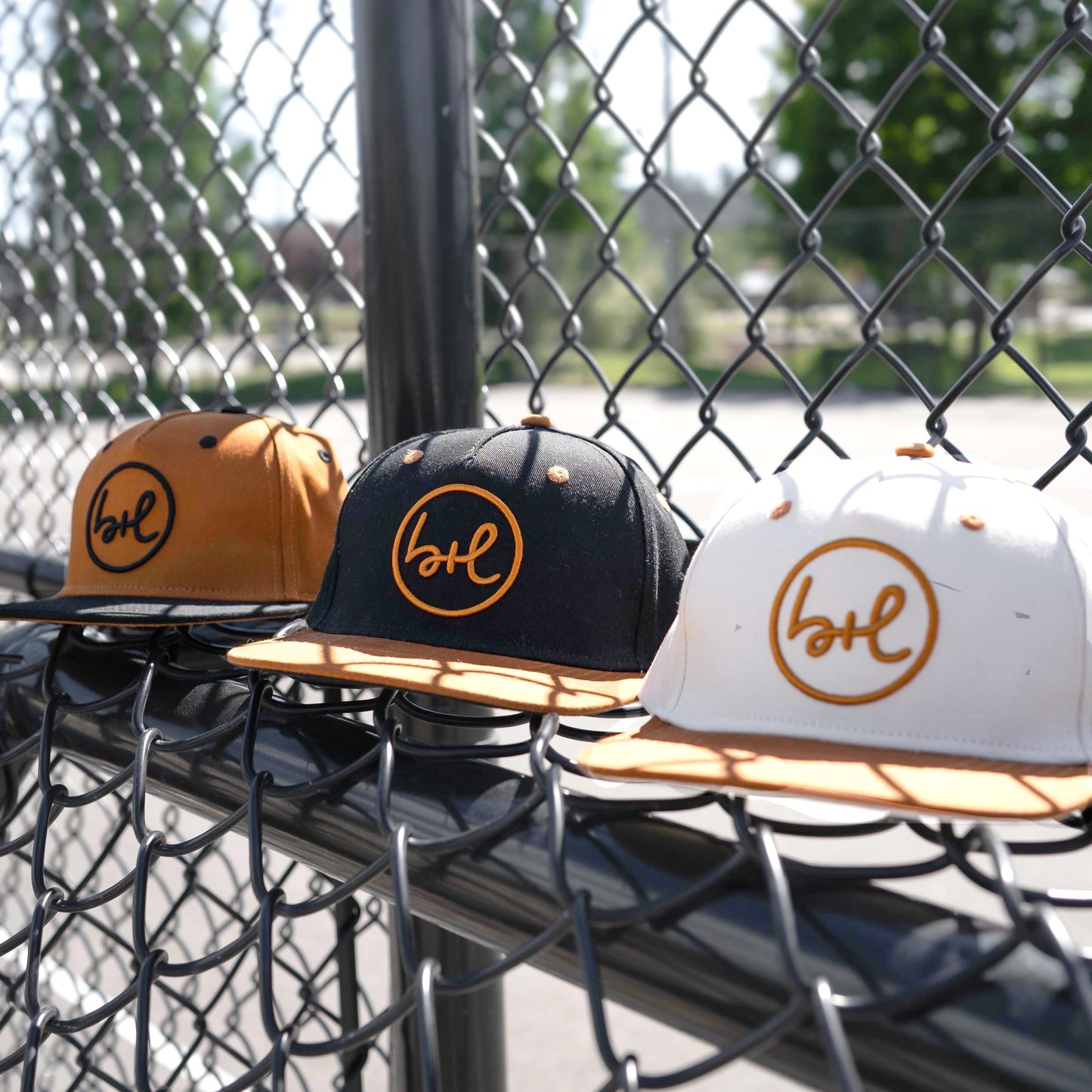 three hats in various colors in front of a chain fence