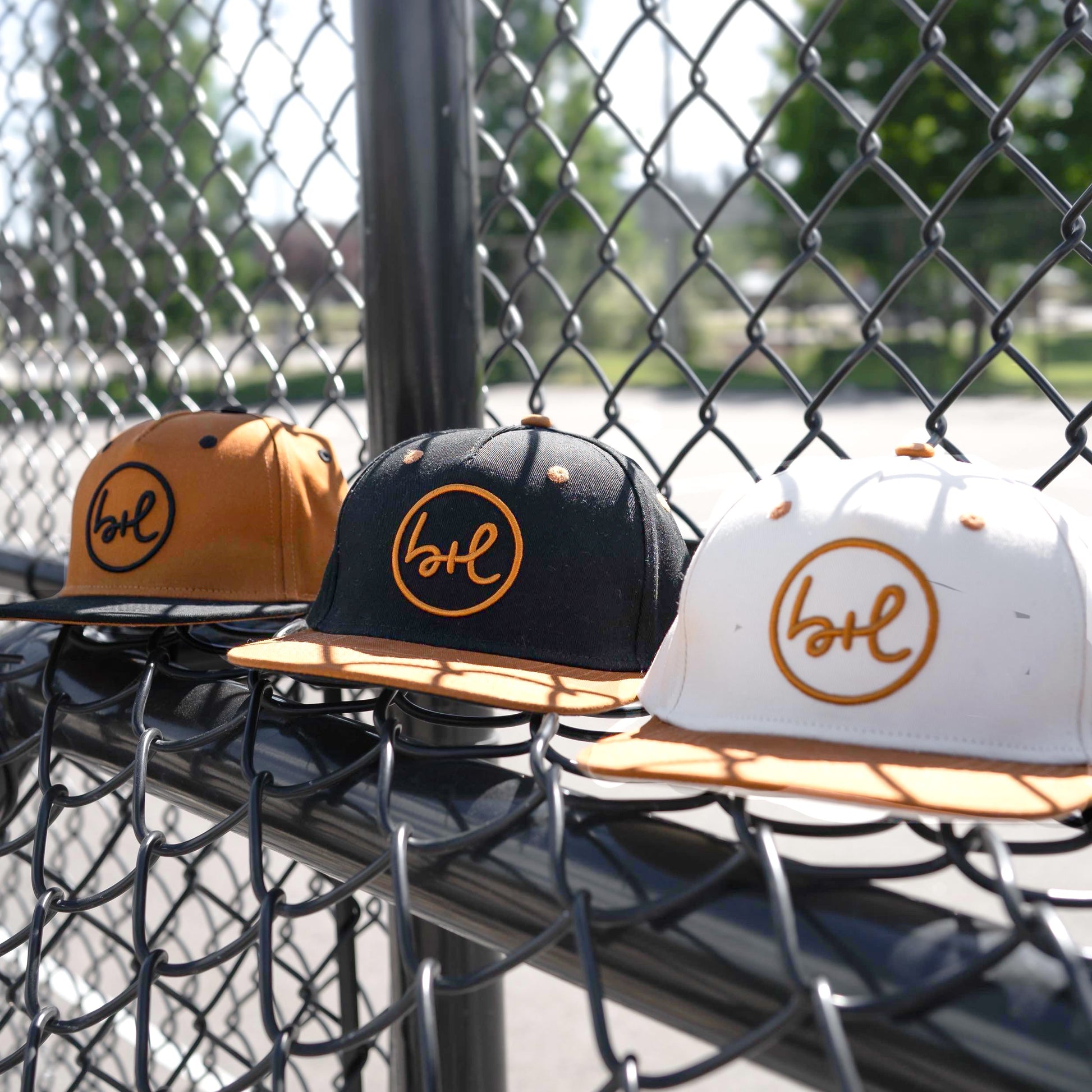 three hats in various colors in front of a chain fence