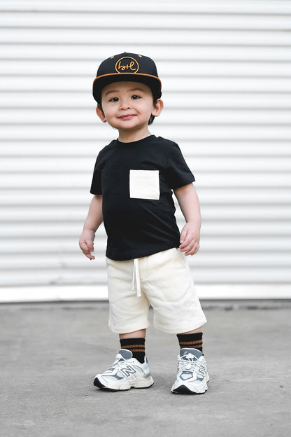 Kid wearing black tee and white shorts with black hat