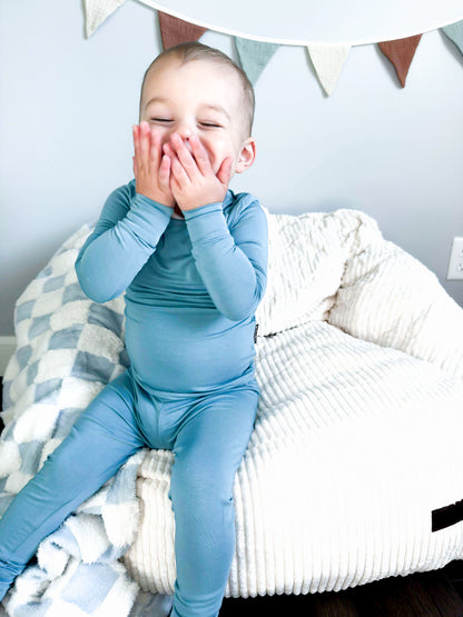 Child wearing a blue outfit sitting on a white cushion with a neutral background