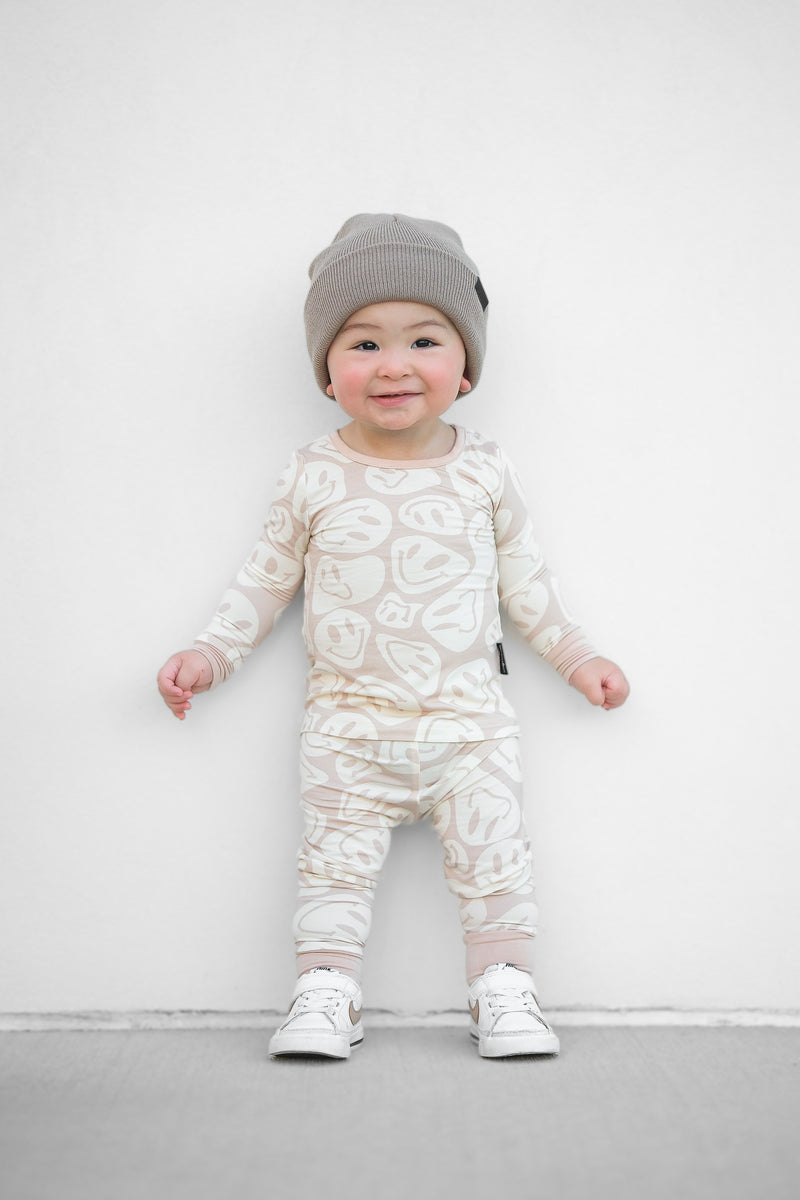 Baby wearing a patterned onesie and gray hat against a white background