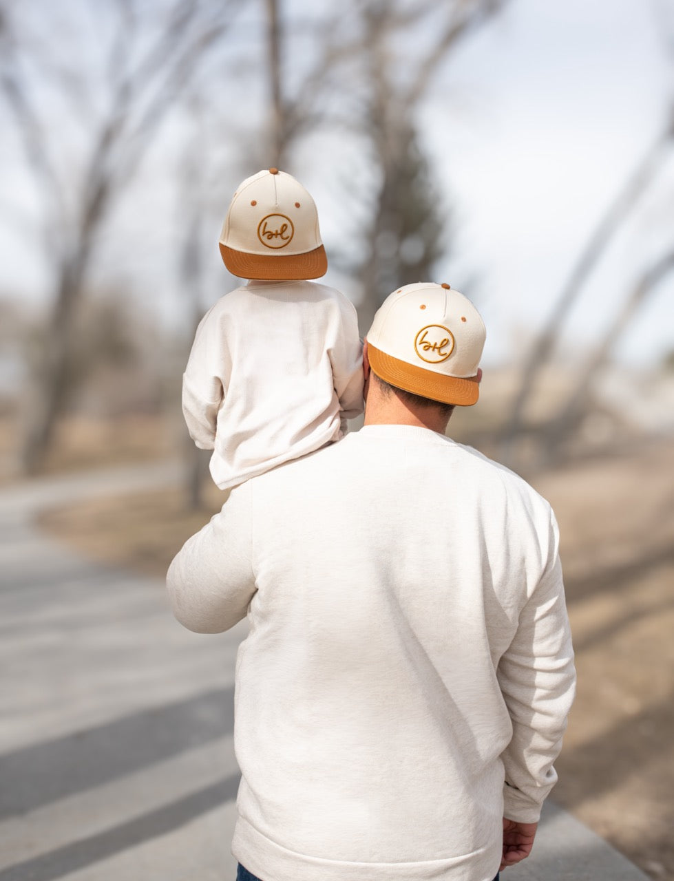 Man and child wearing matching hats and sweatshirts walking together on a path.