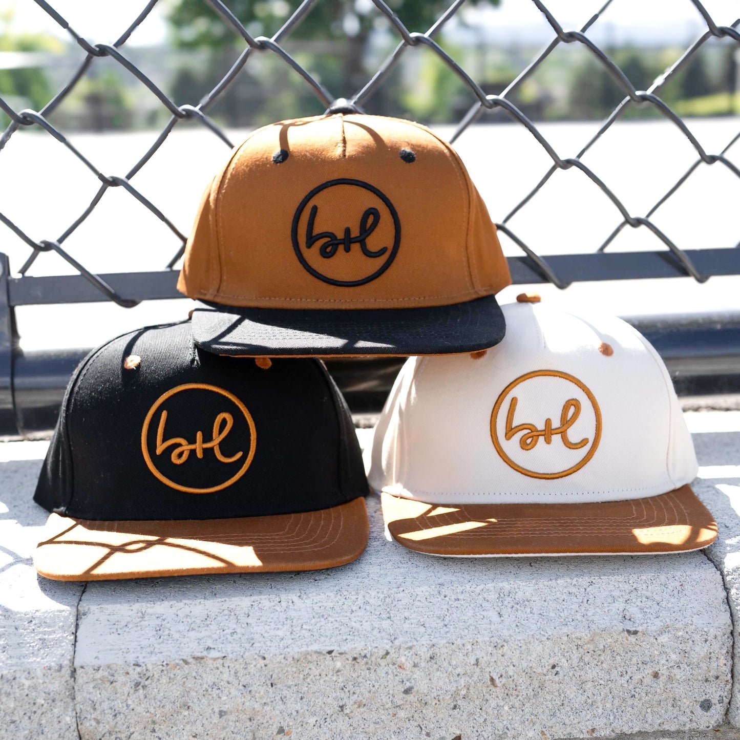 three hats in various colors with brand logo on front in front of a chain fence