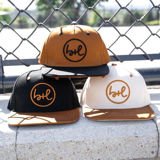 three hats in various colors with brand logo on front in front of a chain fence