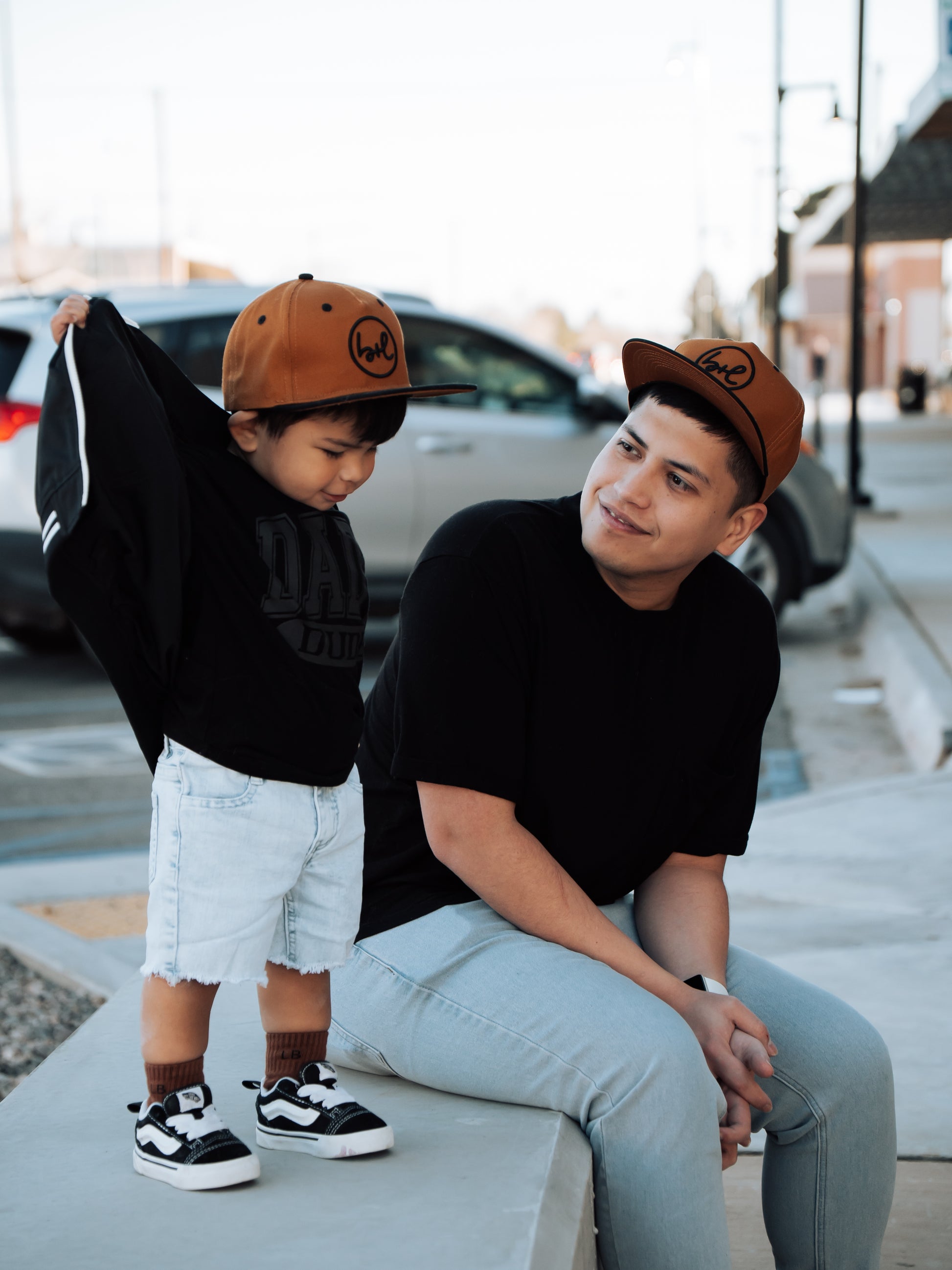 Man and child wearing matching brown caps on a city street.