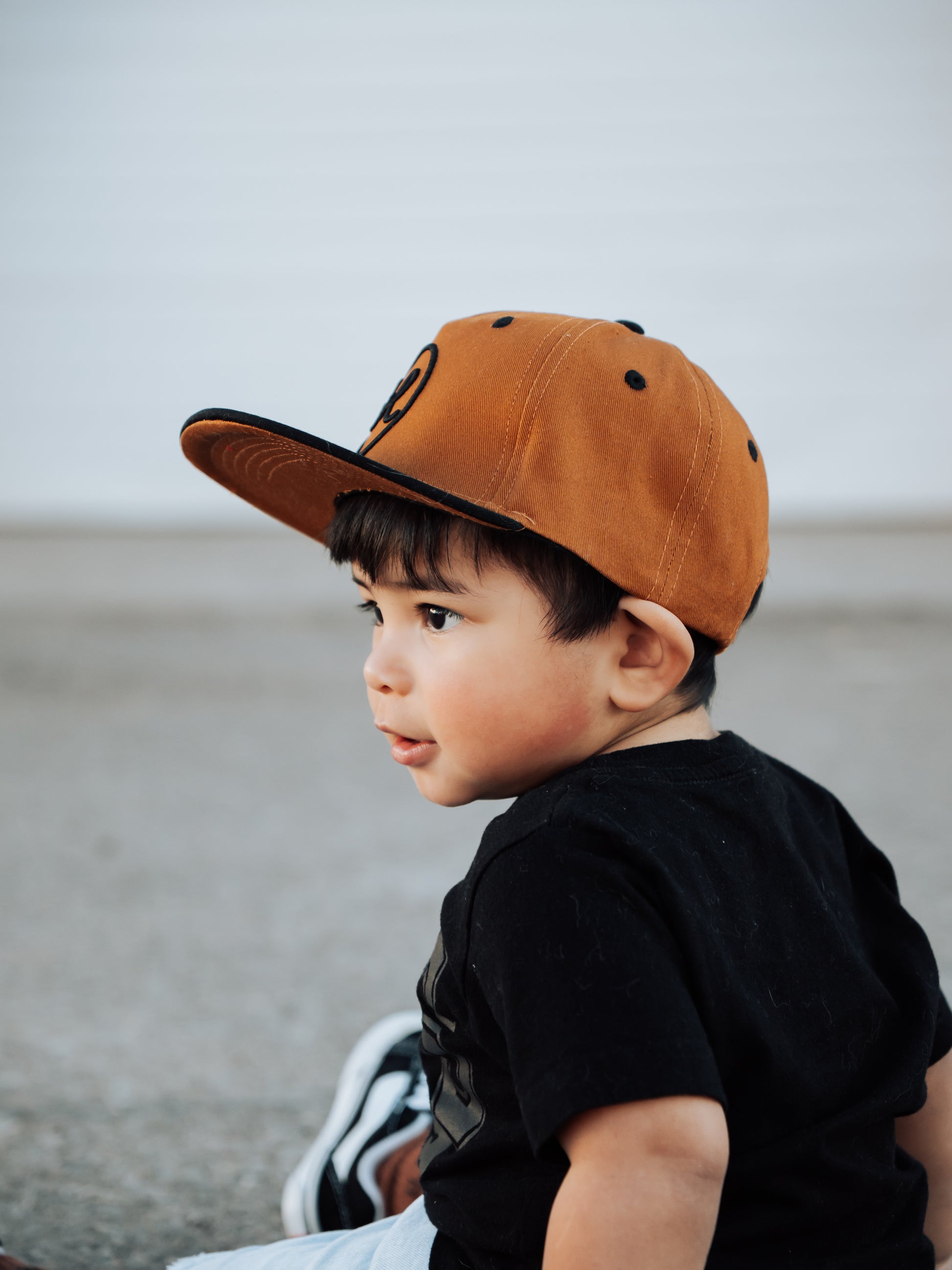 Child wearing a brown cap and black shirt against a neutral background
