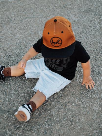 Child wearing an orange and black cap sitting on a concrete surface