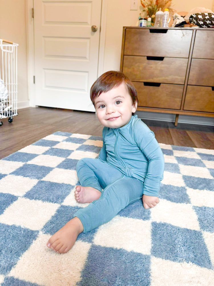 Child sitting on a blue and white checkered rug in a room with wooden furniture.