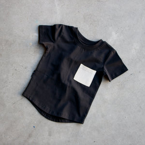 Black t-shirt with a white square patch on a gray concrete floor