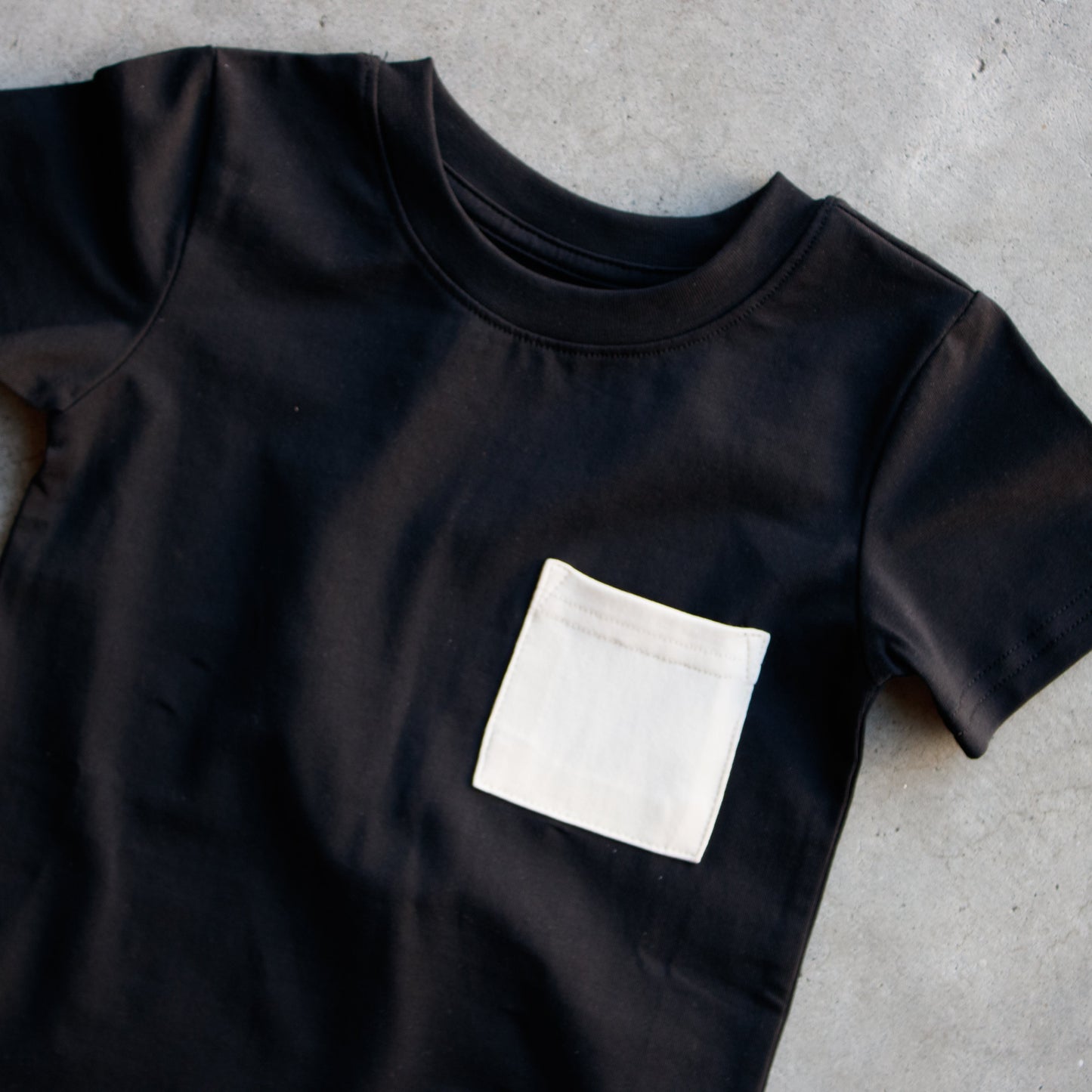 Black t-shirt with a white pocket on a gray concrete surface
