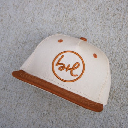 White cap with brown brim and logo on a textured gray surface
