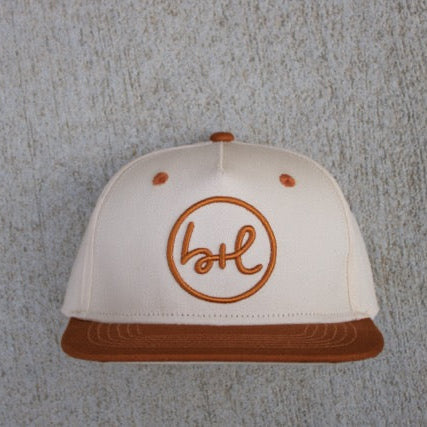 White cap with brown brim and logo on a textured gray background