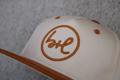 Beige cap with brown embroidered logo on a textured gray background
