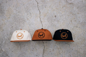 Three caps in white, brown, and black with a logo on a concrete surface